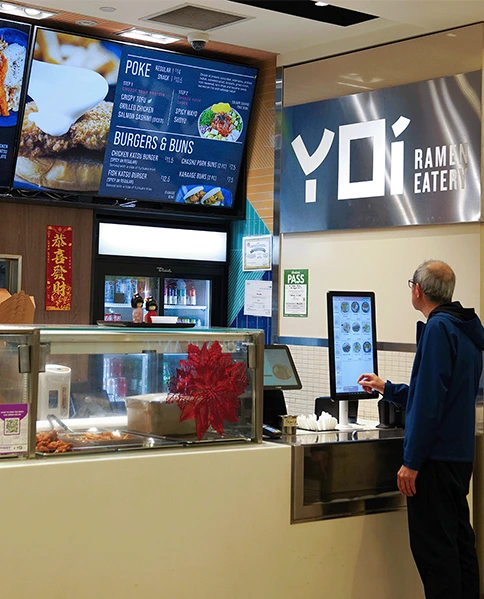 Older man using self-serve kiosk at food hall restaurant